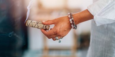 A hand holding a burning sage stick for smudging.