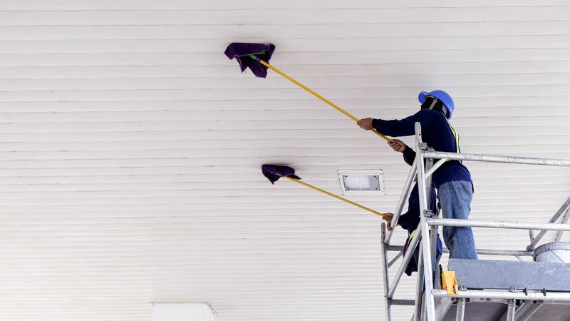 Selective focus at 2 workers on scaffolding using flat wet mops to cleaning white ceiling of petrol station, occupation concept, low angle view copy space