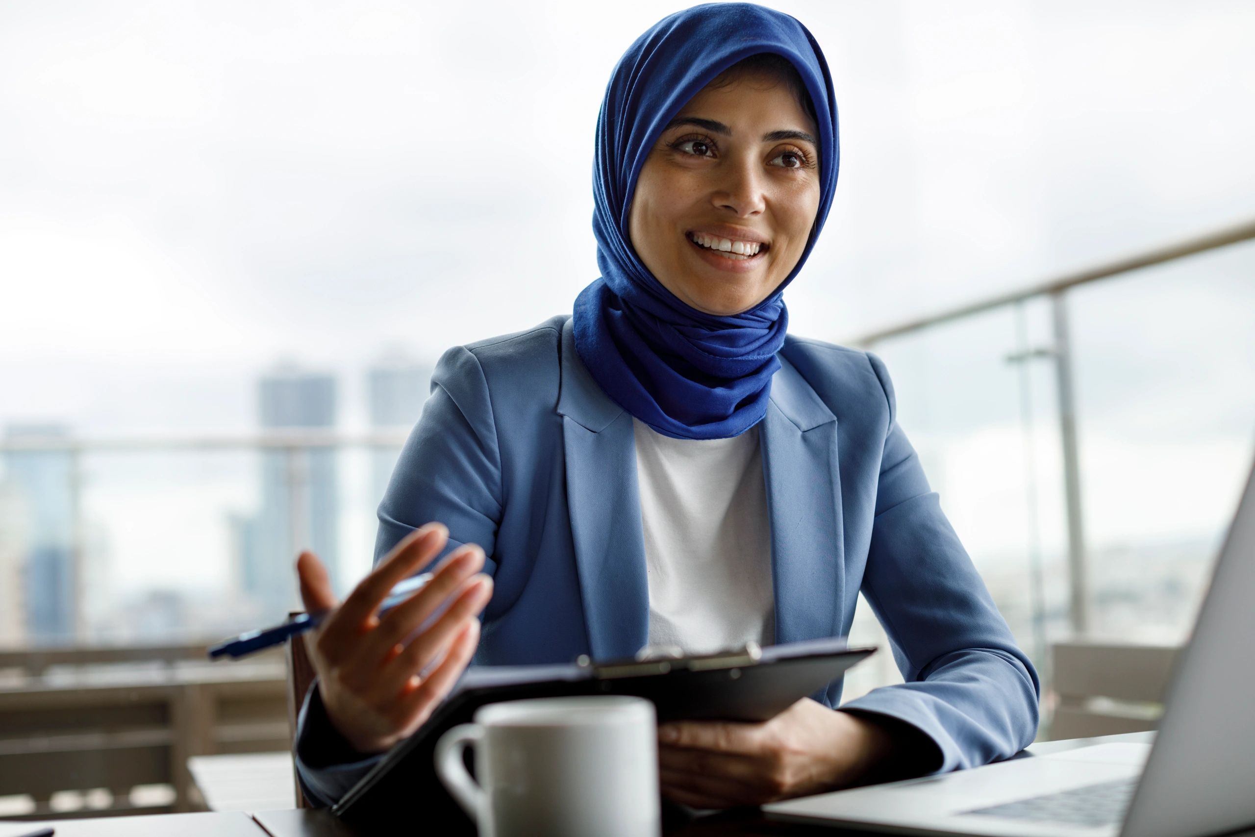 Smiling woman in blue hijab and blazer during a conversation.