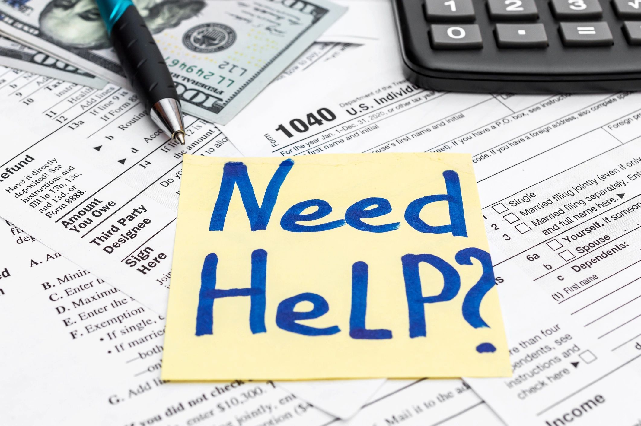 Sticky note saying 'Need Help?' on tax forms with pen, money, and calculator.