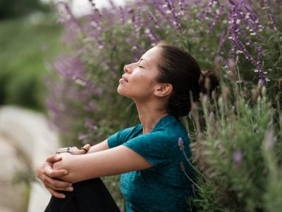 Woman peacefully meditating outdoors surrounded by purple flowers.