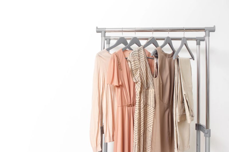 Spring summer beige women's clothing hanging on rail. Calm natural elegant colors. Minimal fashion clothes concept. Female dresses on hanger on white background. Blog, social media hero header