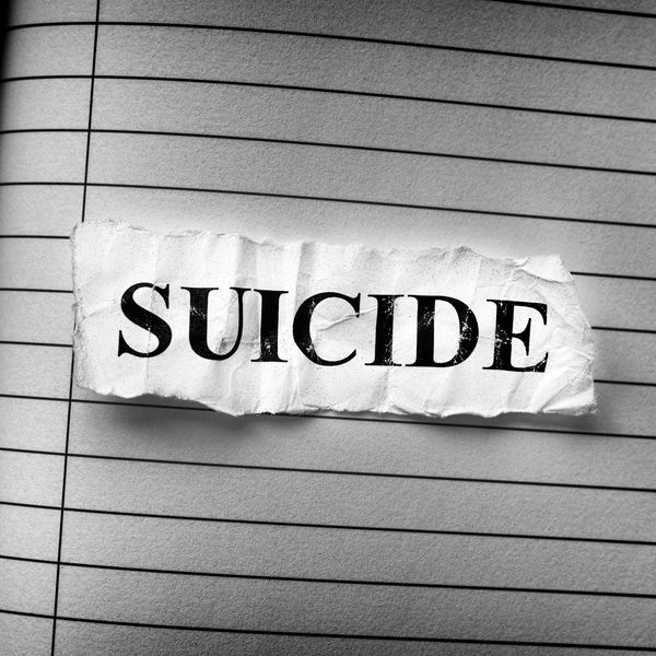 A torn paper with the word 'SUICIDE' on lined paper.
