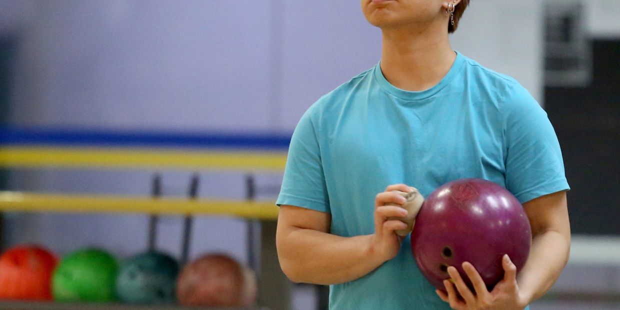 Person holding a purple bowling ball in a bowling alley.
