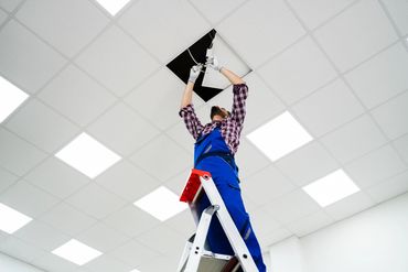 Technician installing a ceiling light while standing on a ladder.