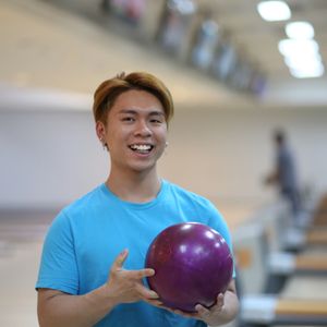 Young man smiling with a bowling ball at a bowling alley.