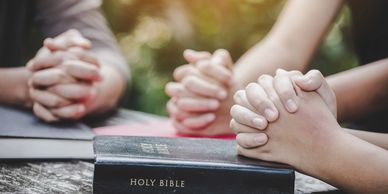 Hands joined in prayer over a Holy Bible.