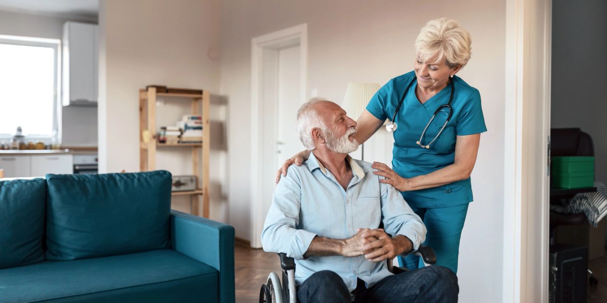 Nurse comforting elderly man in wheelchair at home.