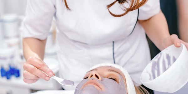 A woman applying a facial mask to a client's face in a spa.