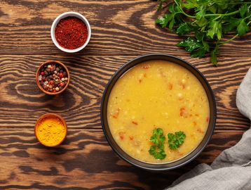 A bowl of creamy lentil soup garnished with parsley on a wooden table.
