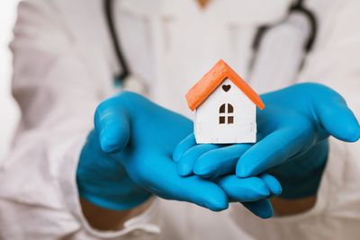 Medical professional holding a small house model with blue gloves.