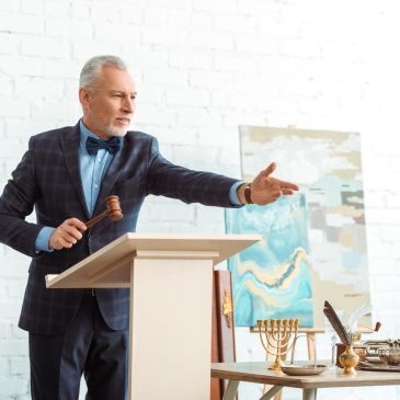 Auctioneer holding gavel and pointing.