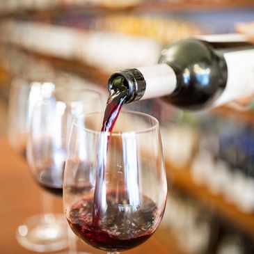 Red wine being poured into a wine glass with other wine glasses blurred in the background