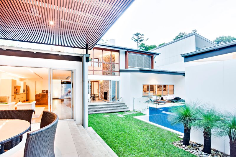 Modern house or hotel indoor outdoor garden and patio area with chairs beside the green grass lawn near to the pool, the enter into the house inside with doors