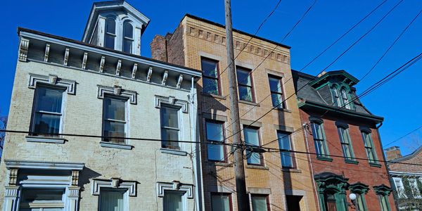 Three historic townhouses with detailed window trims under a clear blue sky.