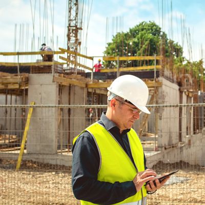 Construction worker wearing safety gear using a tablet on site.