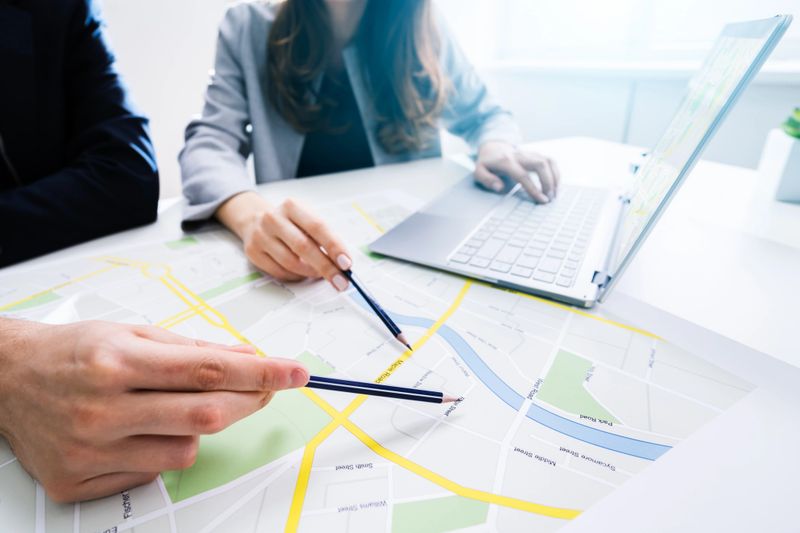 Two People Looking At City Map With Laptop At Table