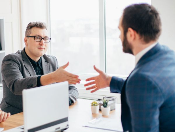 Two businessmen reaching out to shake hands in an office setting.