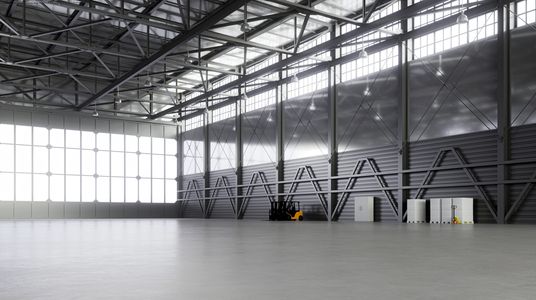 Spacious empty industrial warehouse with high ceilings and large windows.