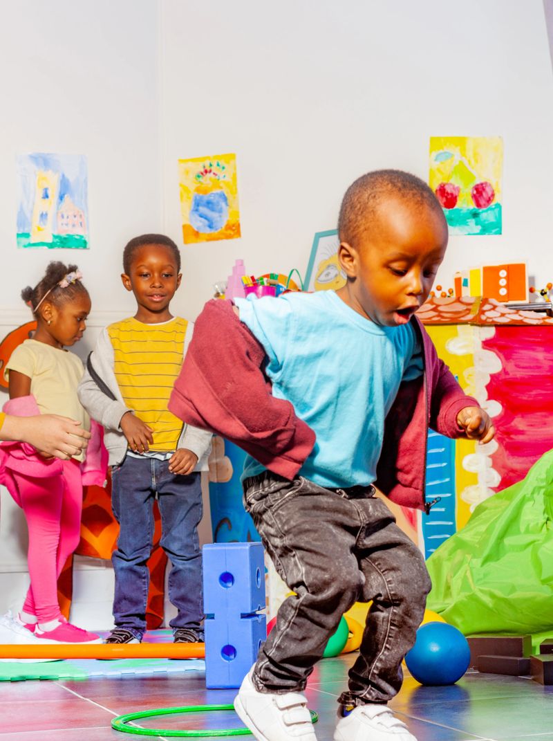 Little black boy jumps from ring to another in physical developmental activity in nursery school with teacher