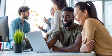 Colleagues collaborating happily on a laptop in a bright office space.