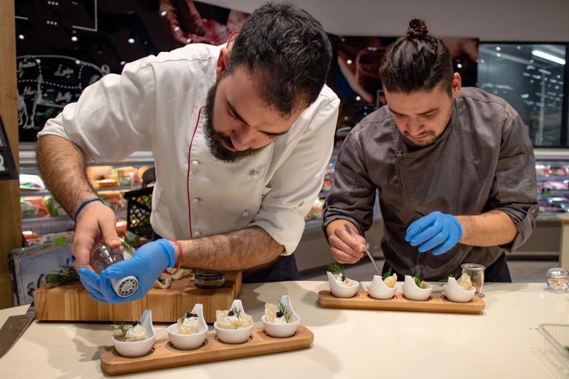 Chefs arranging appetizers on a wooden plate before serving. Teamwork in kitchen. Amuse bouche. Selective focus. Restaurants and fine dining concept.