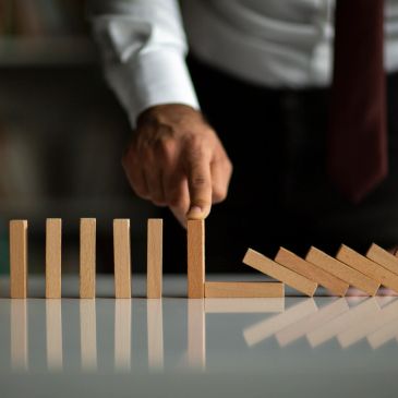 A hand stops falling dominoes by placing a block upright.