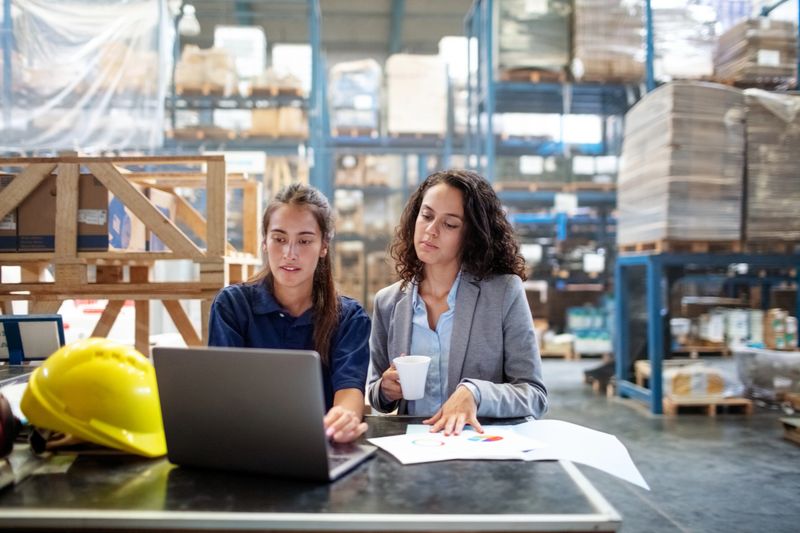 Businesswoman with female worker checking the stocks on laptop computer. Two warehouse employee working on laptop.