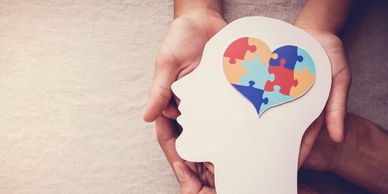 Hands holding a head silhouette with a heart-shaped puzzle inside.