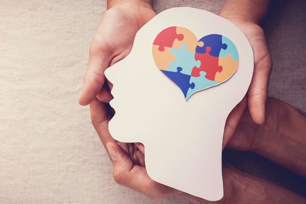 Hands holding a paper cutout of a head with a puzzle heart inside.