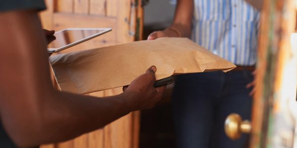 A delivery person hands a brown envelope to a woman at her door.