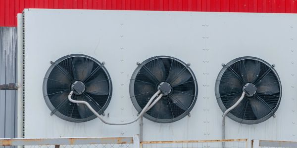 Three large industrial fans mounted on a white wall with red background.