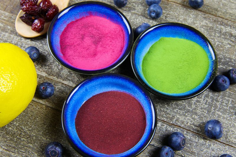 Healthy detox diet concept: bowls with brown aronia powder, green moringa, red beetroot and citrus fruit with blueberries on wood table - Germany