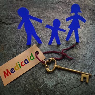 A vintage key with a Medicaid tag and blue paper cutouts of a family on a stone surface.