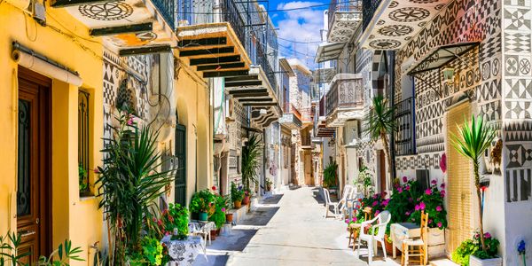 Sunny narrow street with potted plants and patterned balconies in a Mediterranean town.