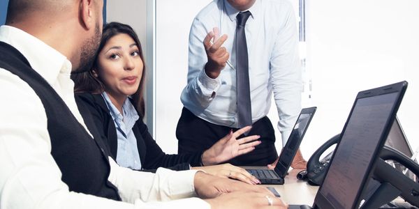 Three colleagues engaged in a discussion around laptops in a modern office.