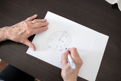 An adult drawing a clock on paper during a cognitive assessment.
