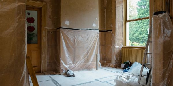 Room under renovation with plastic coverings and a ladder by the window.