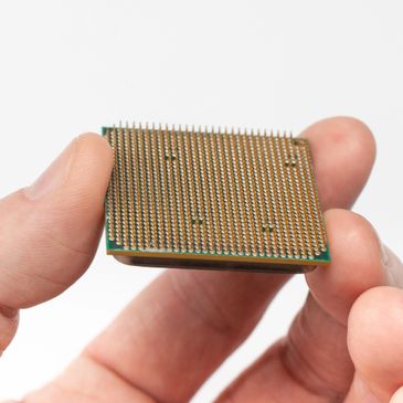 Close-up of a hand holding a computer processor chip with intricate pins.