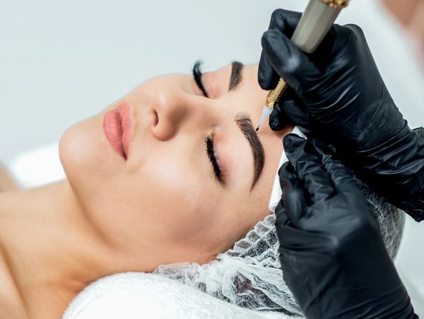 A woman receiving eyebrow microblading treatment in a beauty clinic.