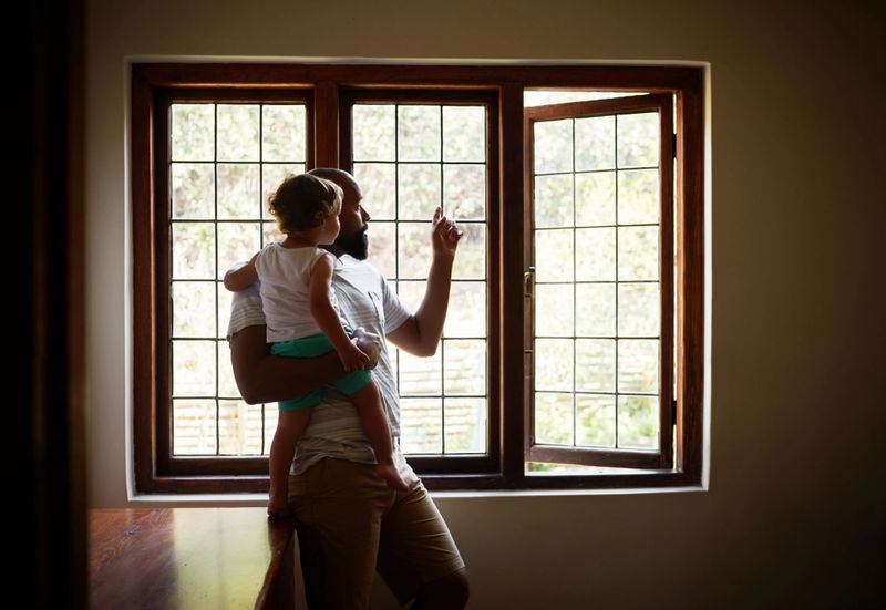Shot of a young man looking out of the window with his adorable child in their new home