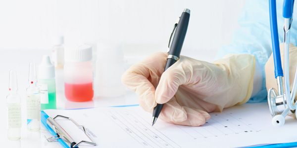 Medical professional writing on a clipboard with test tubes and stethoscope nearby.