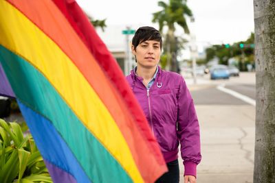 Person holding a rainbow pride flag, wearing a bright pink outfit.