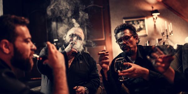 Four men enjoying cigars and drinks in a cozy room filled with smoke.