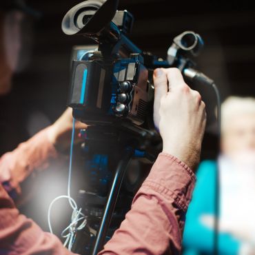 A person filming with a professional video camera indoors.
