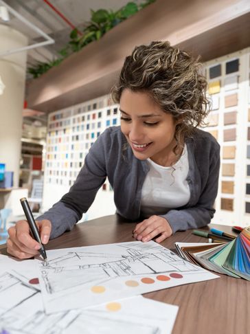 A woman sketches architectural designs with color samples in a creative office.