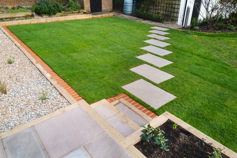 New turf installation around a new stepping stone pathway to a pebbled area and patio with steps. All part of a garden landscaping desing project.