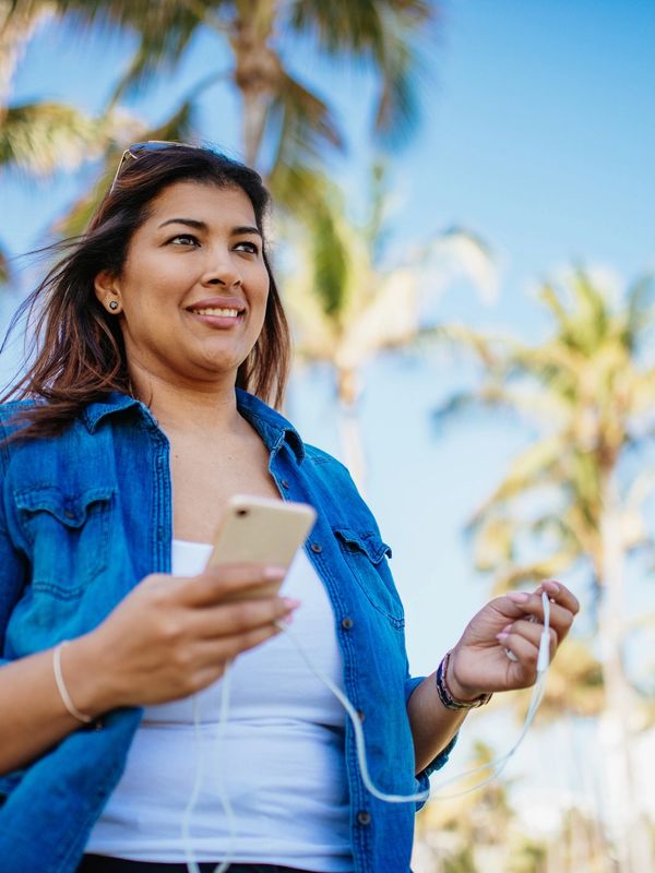 Woman outdoors with phone and earphones under palm trees.