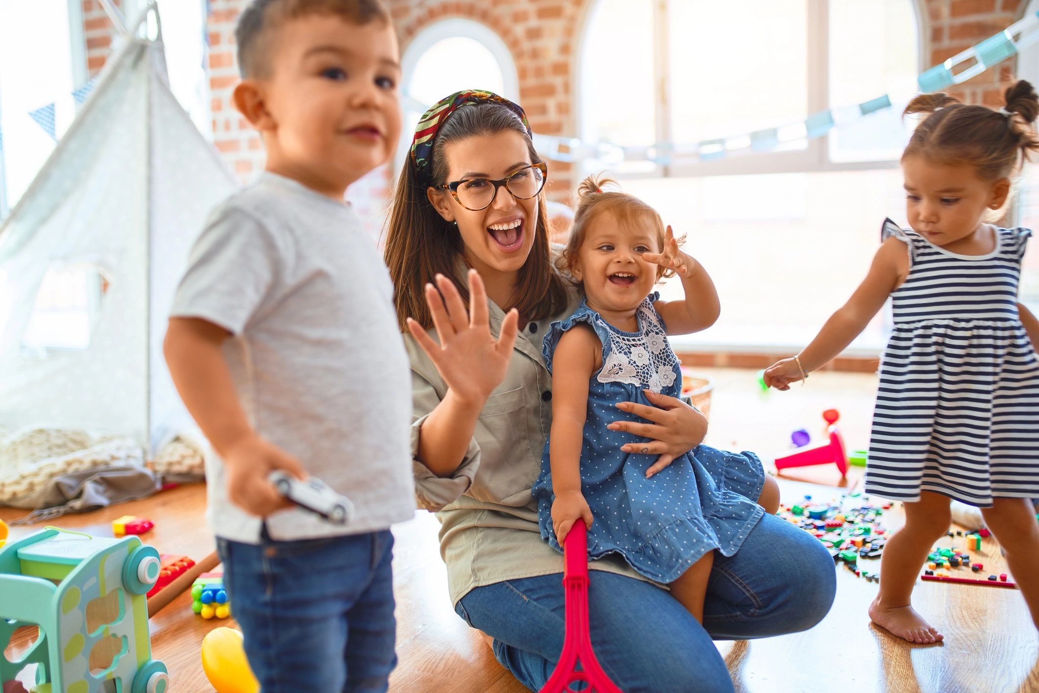 Happy woman and children playing with toys in a bright playroom.