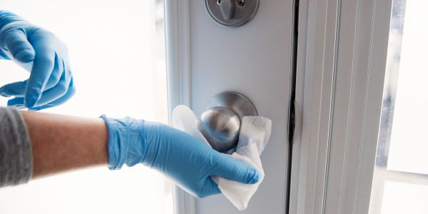 Person disinfecting a door handle with a wipe while wearing gloves.